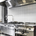 Commercial kitchen with stainless steel appliances and white tiled walls.