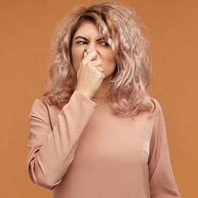 Woman with pink hair covering her mouth against a brown background