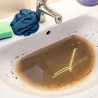 Dirty sink with brown water and a blue cloth on a white countertop.